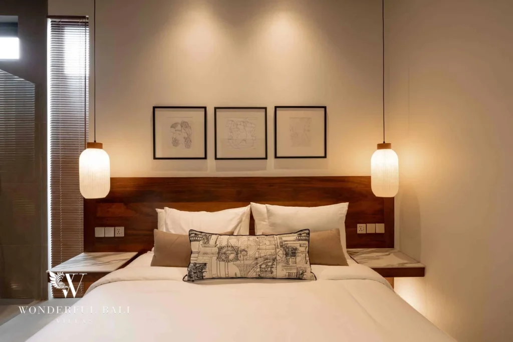 A bedroom with a wooden headboard, framed sketches and warm lantern pendants above a neatly made bed at a 2-bedroom villa in Canggu, Bali