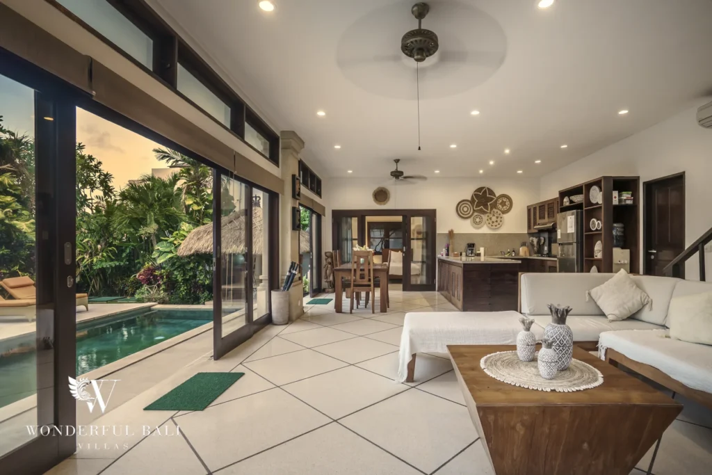 An open-plan living area with a white sofa and wooden coffee table opening through sliding glass doors to the pool at a 4-bedroom villa in Seminyak, Bali