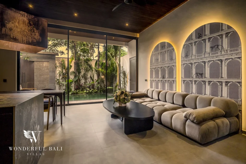 Plush sectional sofa beneath backlit arched architectural murals beside a glass-walled garden view at a 2-bedroom villa in Pererenan, Bali