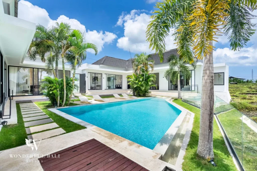 Ground-level view across the private pool and timber deck framed by tall palms and the single-storey villa at a 5-bedroom villa in Pererenan, Bali
