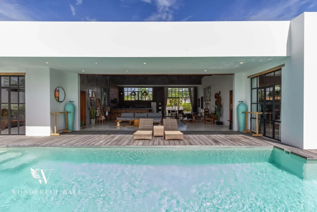 The turquoise pool sits directly in front of an open-sided living area framed by steel-and-glass doors and tall decorative vases at a 3-bedroom villa in Seminyak, Bali