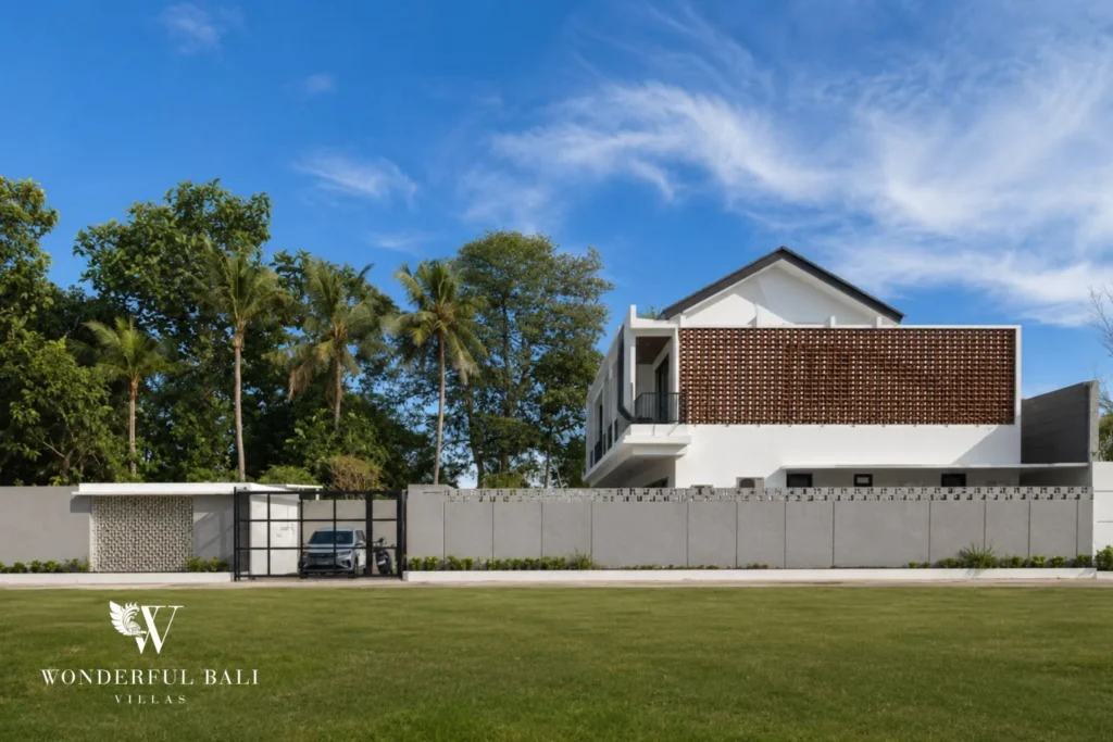 Street view of the contemporary white villa with a woven brick screen and a car parked at the gated entrance at a 4-bedroom villa in Pererenan, Bali
