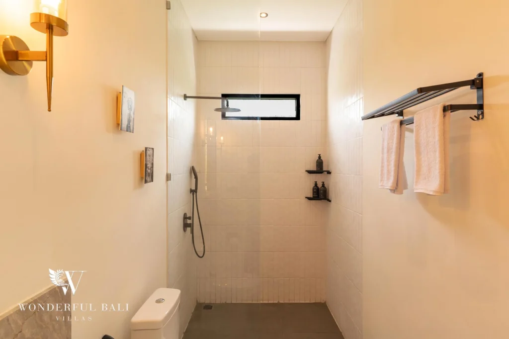 An en-suite walk-in rain shower with white tiling, hanging towels and a toilet at a 2-bedroom villa in Canggu, Bali