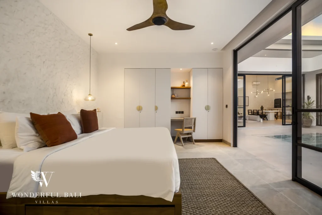 A bedroom with a super-king bed, ceiling fan and built-in wardrobe with a desk nook opening toward the living area at a 3-bedroom villa in Bingin, Uluwatu, Bali
