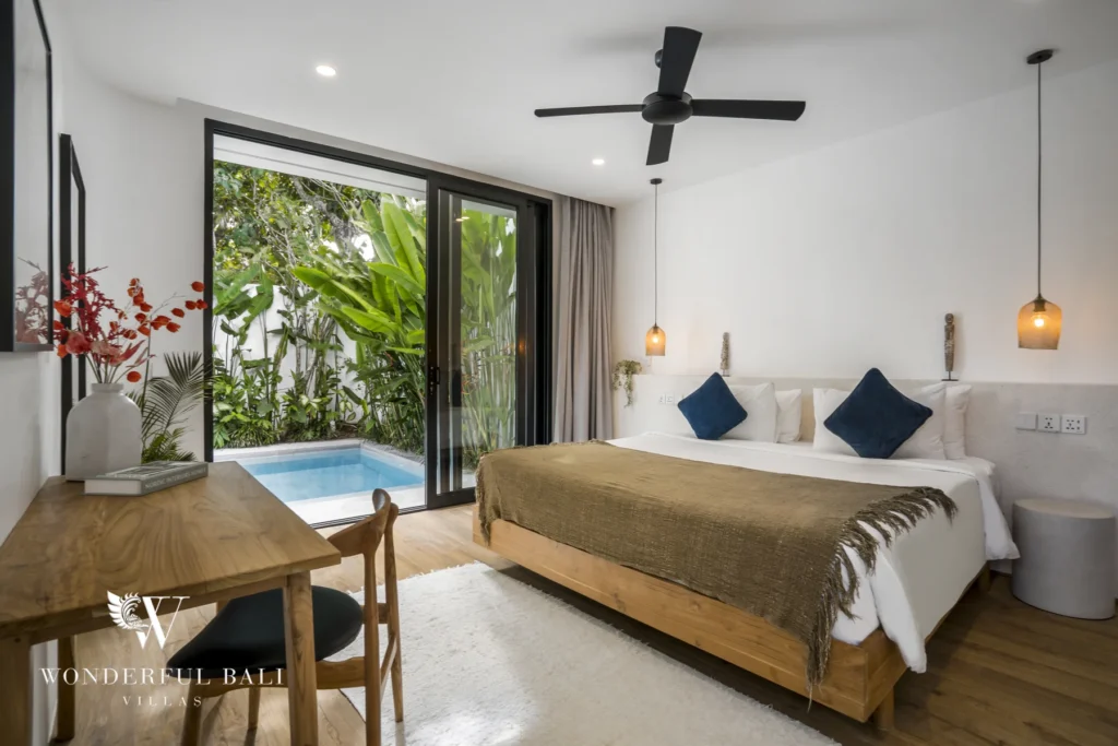 An en-suite bedroom with a wooden bed, ceiling fan and sliding glass doors framing the private pool and tropical foliage at a 3-bedroom villa in Bingin, Uluwatu, Bali