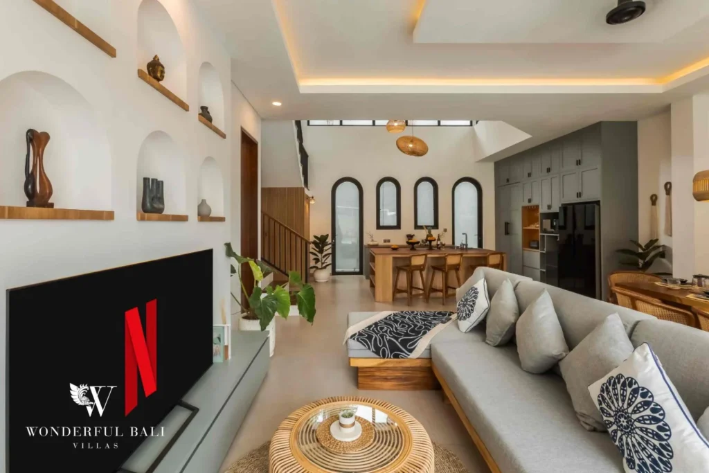 A bright double-height living area with a grey sofa, arched alcove shelving and an open kitchen beyond at a 4-bedroom villa in Pererenan, Bali