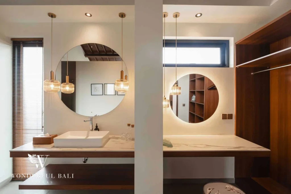 A double vanity with two round mirrors, amber pendants and an adjoining wooden wardrobe at a 2-bedroom villa in Canggu, Bali
