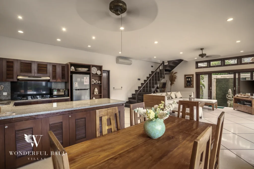 A wooden kitchen with granite island and dining table beside a staircase and living area at a 4-bedroom villa in Seminyak, Bali