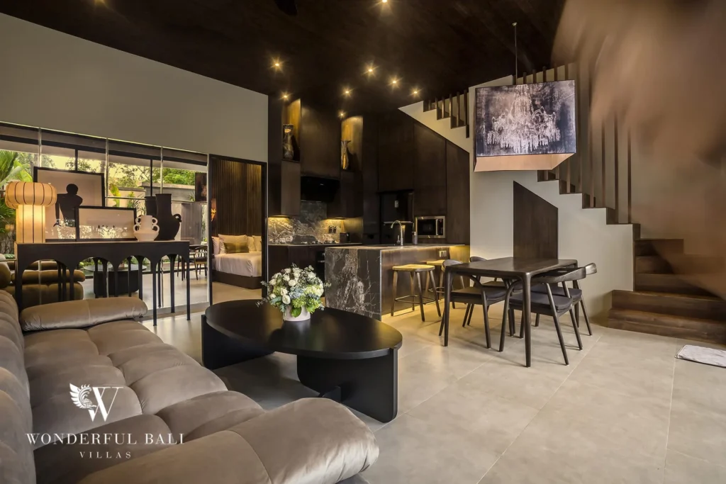 Lofty double-height living and dining area with staircase, dark kitchen and neutral sofas at a 2-bedroom villa in Pererenan, Bali