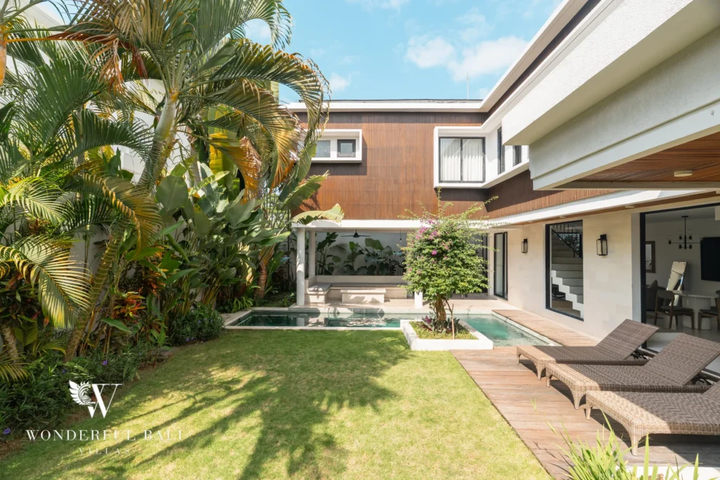A private swimming pool, grassy tropical garden with palms and rattan sun loungers set against the two-storey villa facade at a 3-bedroom villa in Berawa, Bali