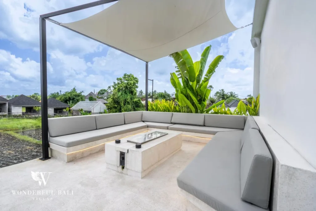 Shaded rooftop lounge with grey L-shaped sofas and a stone fire-pit table overlooking the neighbourhood at a 5-bedroom villa in Pererenan, Bali