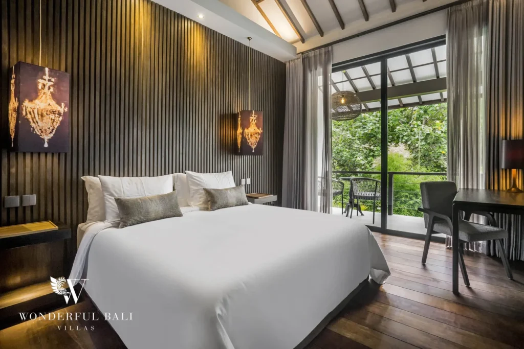 A bedroom with a white bed, dark slatted feature wall and sliding glass doors opening to a private balcony and desk at a 3-bedroom villa in Pererenan, Bali