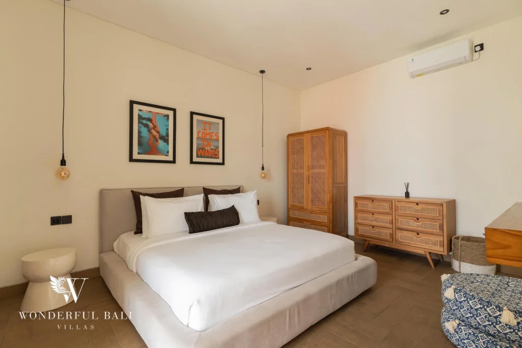 A bright bedroom with a low double bed, rattan wardrobe and dresser and framed surf prints at a 2-bedroom villa in Canggu, Bali