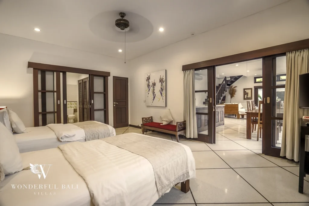 A bright twin-bed bedroom overlooking the dining area and staircase through sliding glass doors at a 4-bedroom villa in Seminyak, Bali