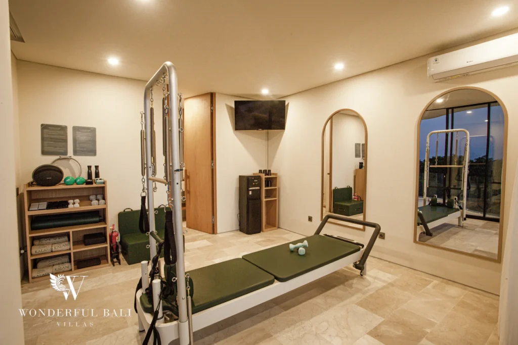 A fully equipped gym with a reformer, dumbbells, storage shelves and arched mirrors under warm lighting at a 3-bedroom villa in Bingin, Uluwatu, Bali
