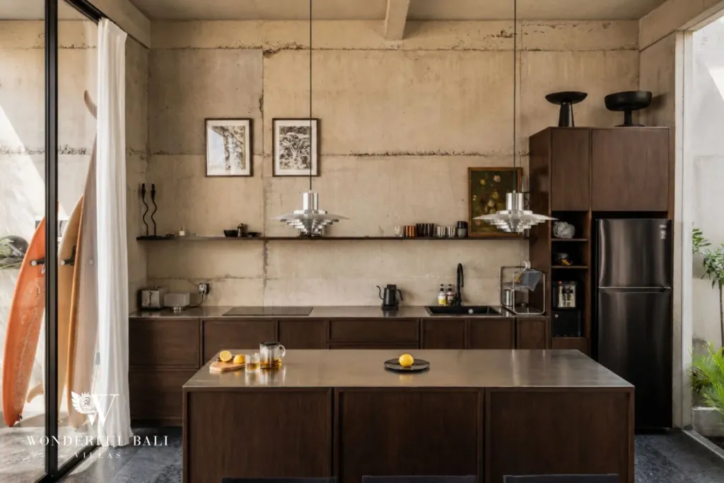 Industrial kitchen with dark timber cabinetry, a stone-topped island, pendant lights and a surfboard leaning against the concrete wall at a 2-bedroom villa in Seseh, Bali