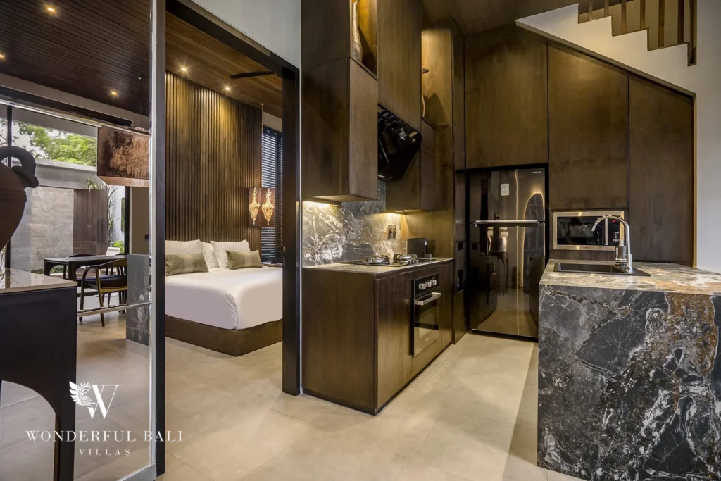Fully equipped kitchen with marble island, dark cabinetry and integrated appliances beside a bedroom at a 2-bedroom villa in Pererenan, Bali