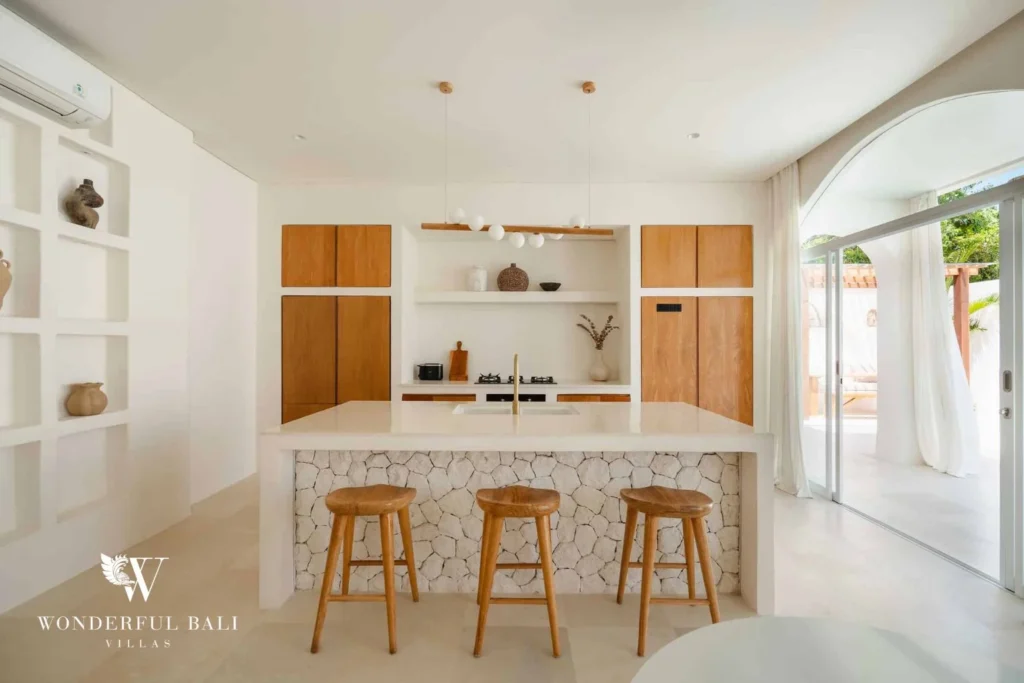 A fully equipped modern kitchen with a stone-clad island, wooden bar stools, timber cabinetry and pendant lighting, at a 2-bedroom villa in Bingin, Uluwatu, Bali