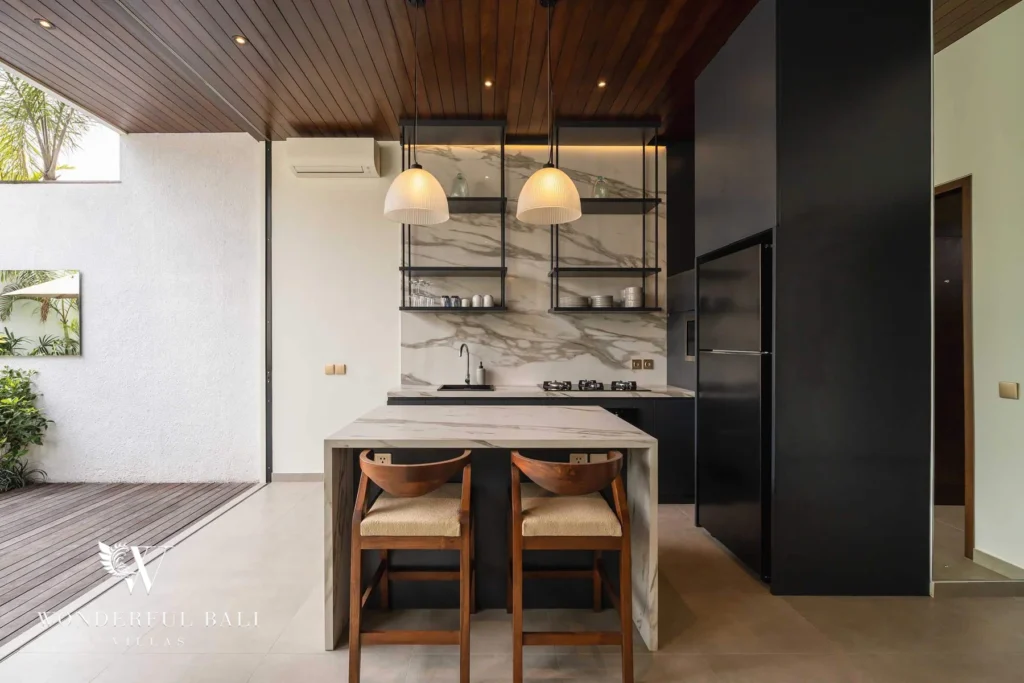 A marble kitchen island with wooden bar stools, black cabinetry and a fridge opening to the deck at a 2-bedroom villa in Canggu, Bali
