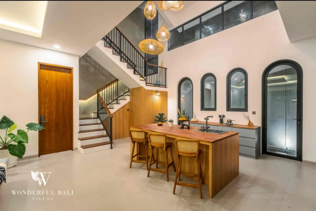 A timber breakfast-bar island beneath the staircase with rattan stools and arched black-framed doorways at a 4-bedroom villa in Pererenan, Bali