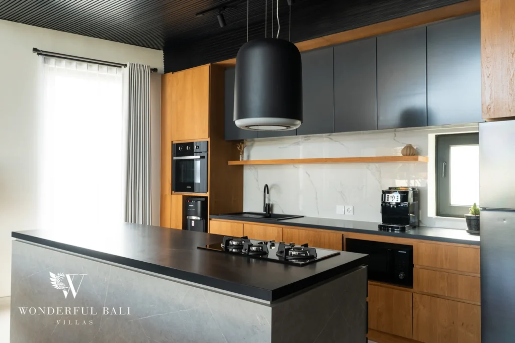 A high-end kitchen with a stone island, gas cooktop, marble backsplash, dark cabinetry, timber units and an espresso machine at a 5-bedroom villa in Batu Bolong, Canggu, Bali