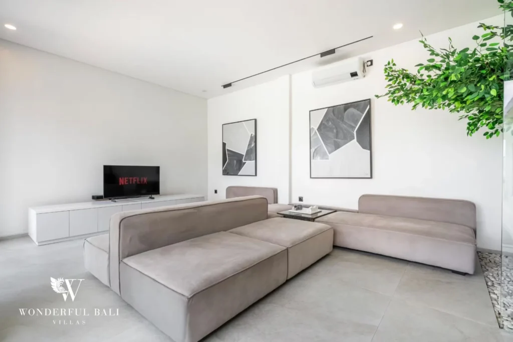 Open living room with a large taupe modular sofa, wall-mounted TV and framed abstract art at a 5-bedroom villa in Pererenan, Bali
