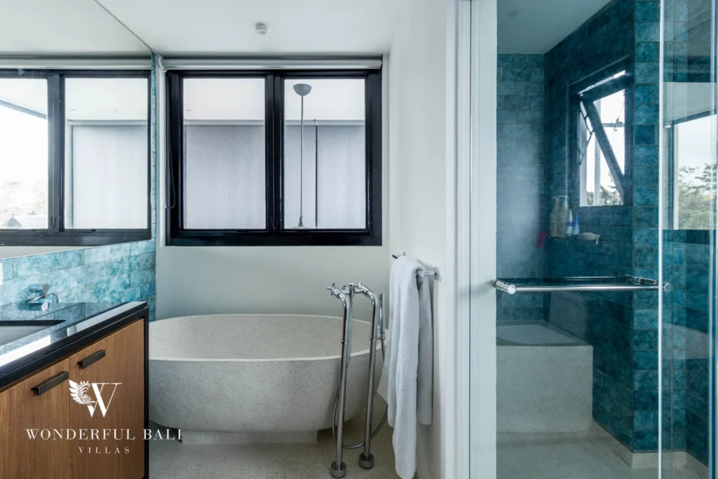 A bathroom with a freestanding stone bathtub, teal-tiled walk-in shower and a timber vanity beneath black-framed windows at a 4-bedroom villa in Batu Bolong, Canggu, Bali