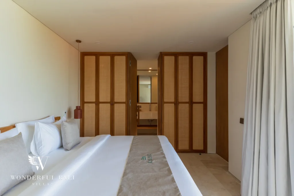 A bedroom with a large bed, woven rattan wardrobes and a glimpse of the ensuite bathroom beyond at a 3-bedroom villa in Bingin, Uluwatu, Bali
