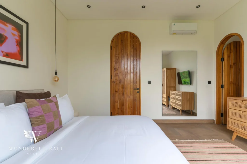 A second bedroom with a white-linen bed, arched timber doors and a full-length mirror at a 2-bedroom villa in Canggu, Bali