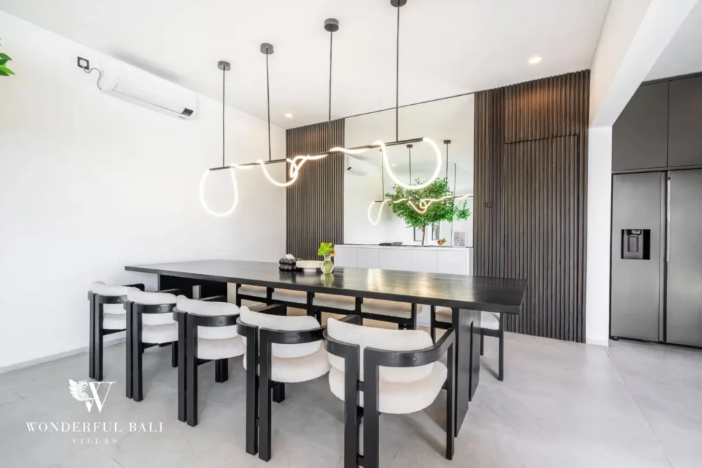 Modern dining area with a black table, boucle chairs, sculptural light fixture and fluted wood feature wall at a 5-bedroom villa in Pererenan, Bali