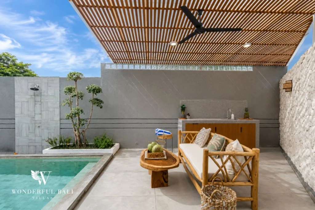 A covered timber-slat pergola lounge beside the pool with a bamboo daybed and outdoor shower at a 4-bedroom villa in Pererenan, Bali