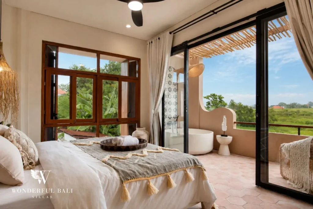 A queen bedroom opening to a terrace bathtub and rice-field views through sliding glass doors at a 3-bedroom villa in Pererenan, Bali