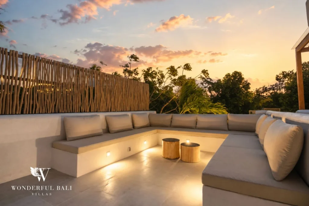 A rooftop lounge with an L-shaped cushioned bench and glowing side tables against a golden sunset sky, at a 2-bedroom villa in Bingin, Uluwatu, Bali