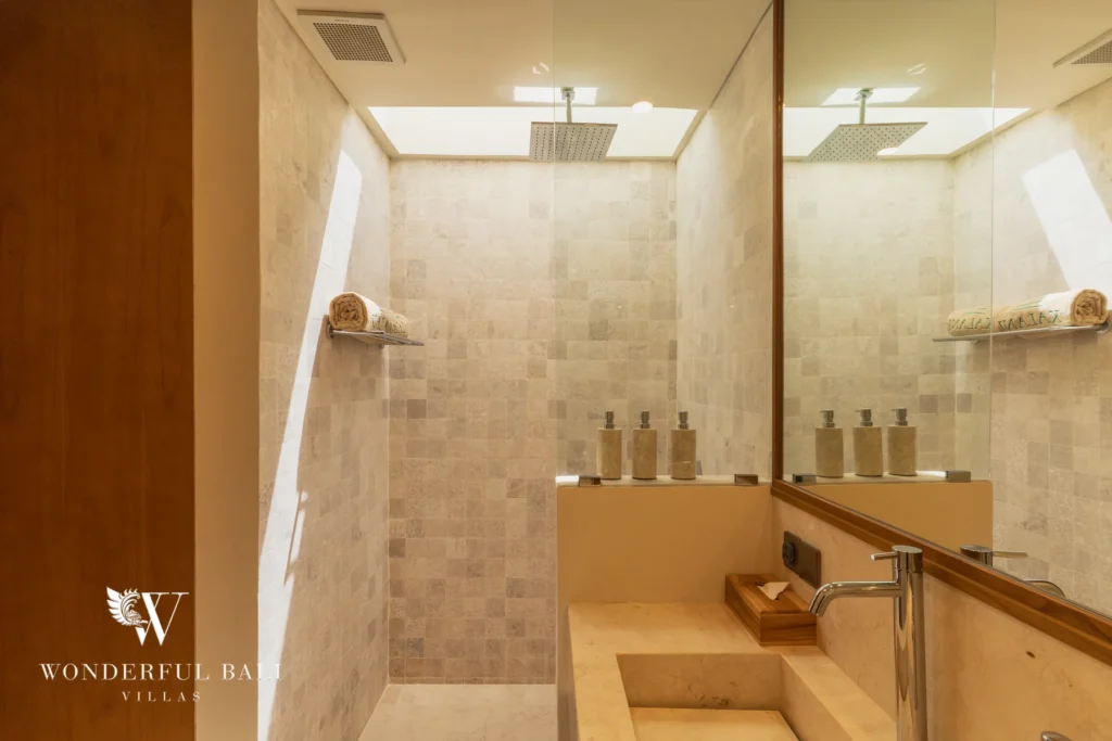 A stone-tiled bathroom with a walk-in rain shower and a sculpted stone vanity basin at a 3-bedroom villa in Bingin, Uluwatu, Bali