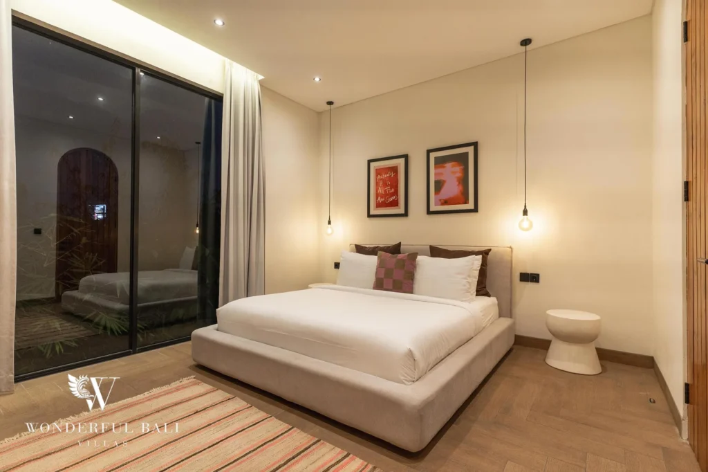 A second bedroom lit at night with a double bed and glass sliding doors opening to the pool garden at a 2-bedroom villa in Canggu, Bali