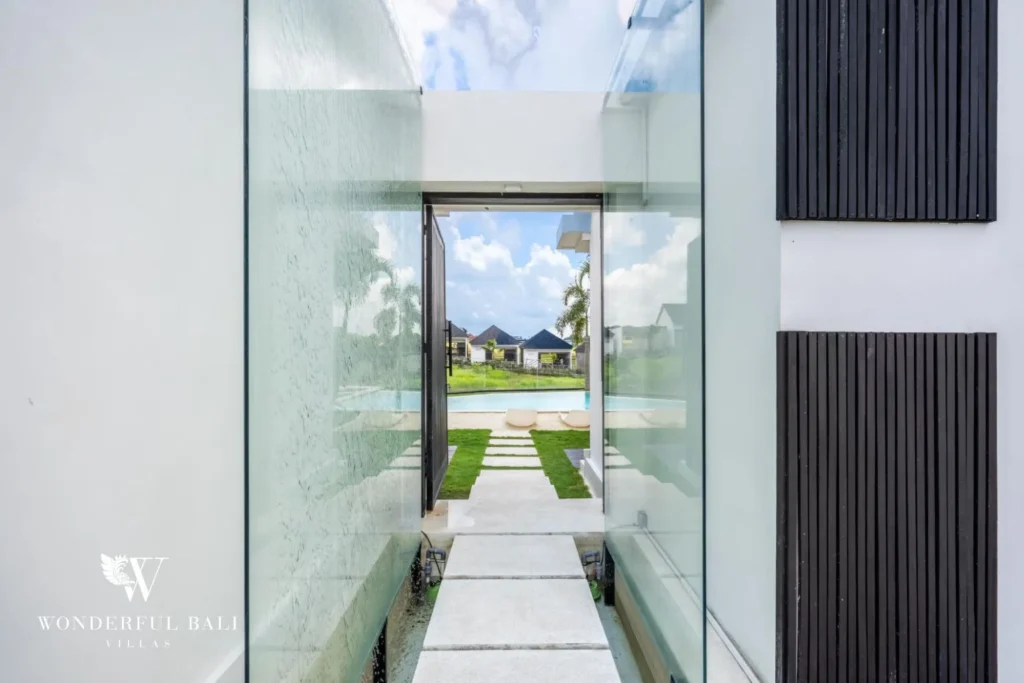 Glass-walled entrance corridor leading out toward the pool and garden at a 5-bedroom villa in Pererenan, Bali