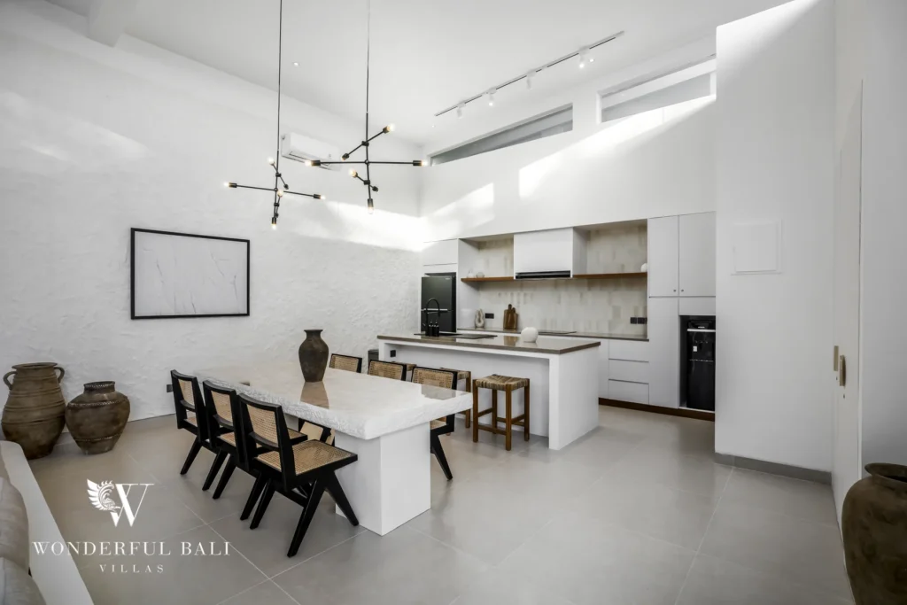A fully equipped white kitchen with a dining table seating six and a sculptural pendant light at a 3-bedroom villa in Bingin, Uluwatu, Bali