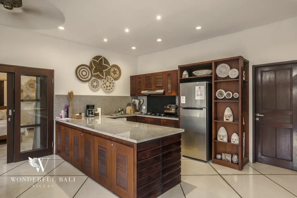 A fully equipped wooden kitchen with granite counters, stainless refrigerator and decorative wall baskets at a 4-bedroom villa in Seminyak, Bali