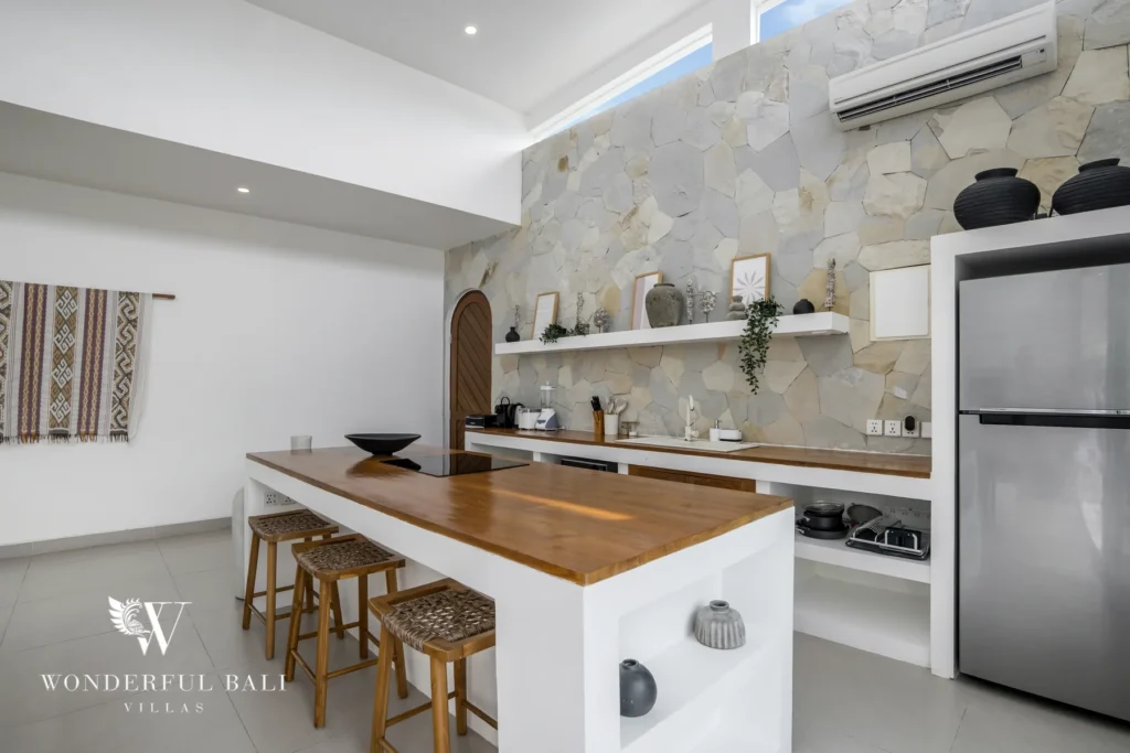 Fully equipped kitchen with a wooden-topped island, rattan bar stools and a natural stone feature wall at a 3-bedroom villa in Bingin, Uluwatu, Bali