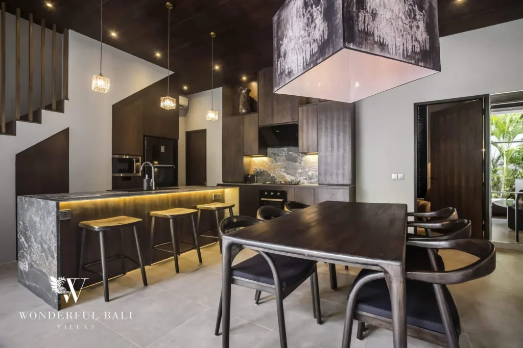 A fully equipped modern kitchen with a marble island, bar stools, dark cabinetry and an adjacent dark timber dining table at a 3-bedroom villa in Pererenan, Bali