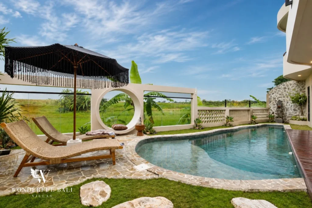 A curved pool and sun loungers set against open rice fields with a round decorative window at a 3-bedroom villa in Pererenan, Bali