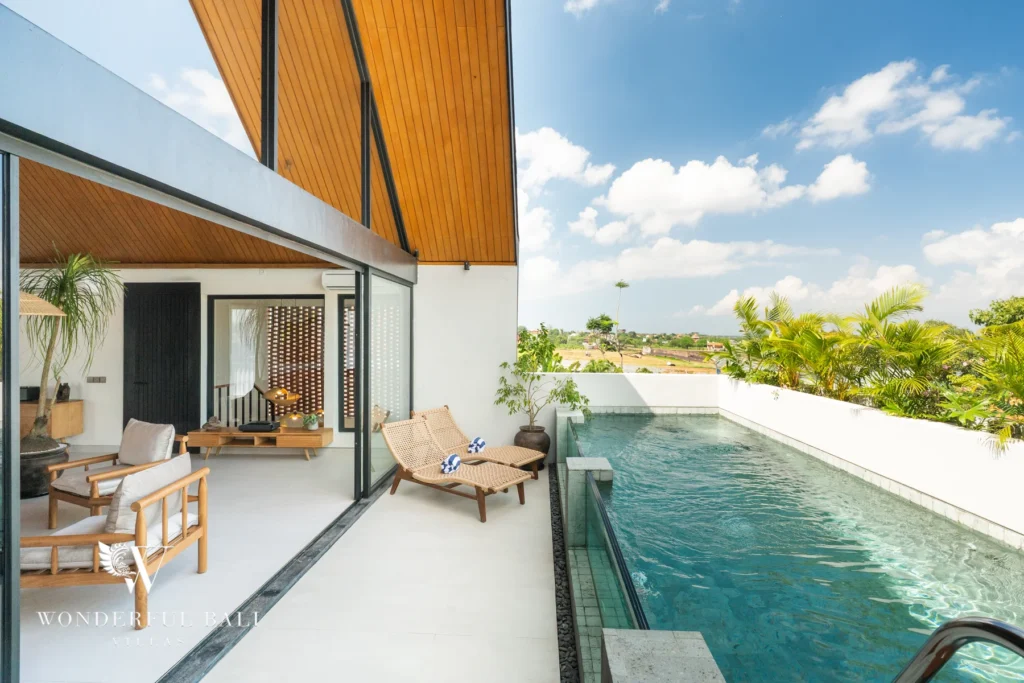 A rooftop pool running alongside a covered terrace with timber loungers and armchairs beneath a peaked wooden roof, overlooking rice fields at a 5-bedroom villa in Batu Bolong, Canggu, Bali