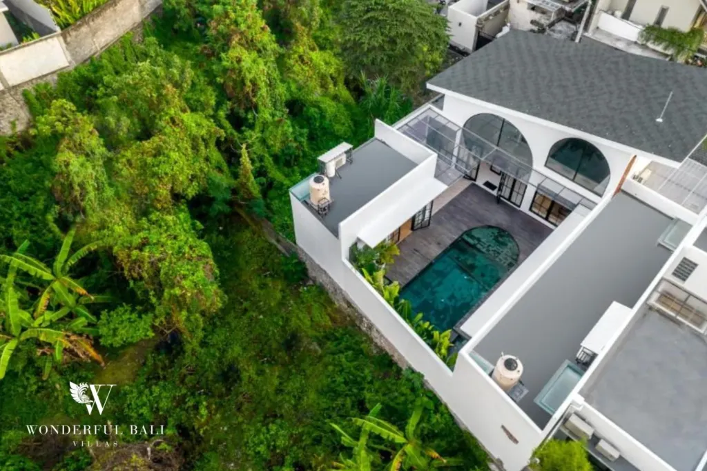 An aerial view of the villa's black-shingle roof, courtyard pool, and surrounding lush green jungle at a 3-bedroom villa in Pererenan, Bali