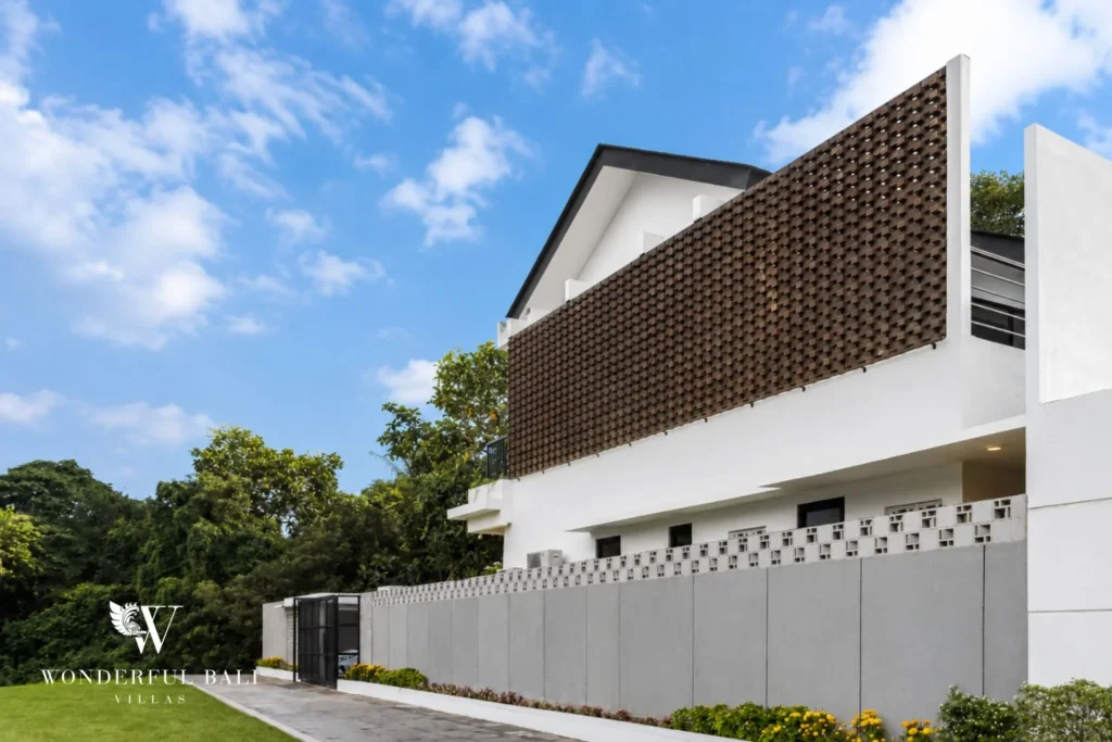 Side elevation of the white villa showing the upper woven-brick screen and perimeter wall along the driveway at a 4-bedroom villa in Pererenan, Bali