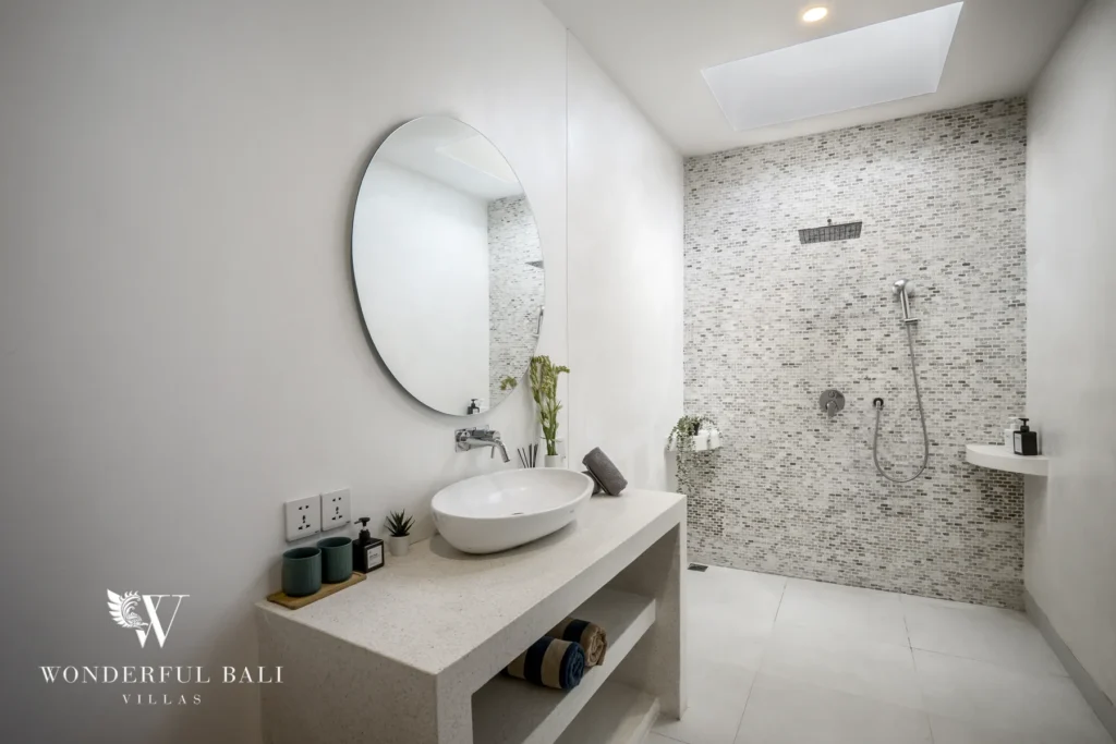 A bright bathroom with a terrazzo vanity, oval mirror and mosaic-tiled walk-in shower at a 3-bedroom villa in Bingin, Uluwatu, Bali