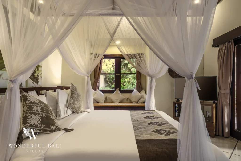A canopy bed draped in white mosquito netting with a window daybed and traditional cushions at a 4-bedroom villa in Seminyak, Bali