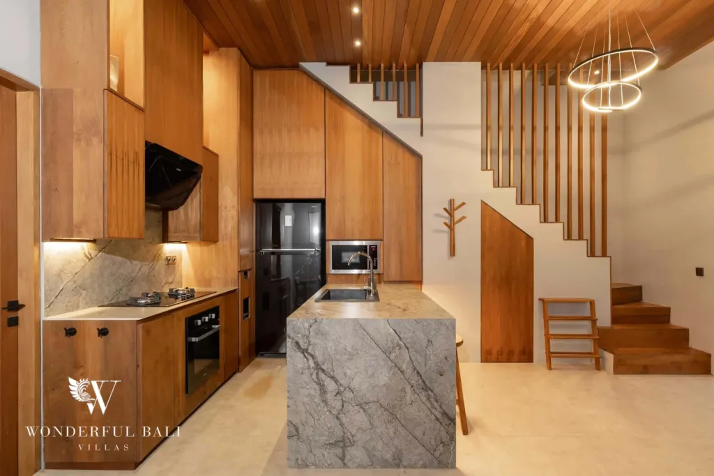 2BR villa for rent in Pererenan — kitchen, a gourmet kitchen with a grey stone island, timber cabinetry, gas hob and a floating wood staircase beneath a ring chandelier at a 2-bedroom villa