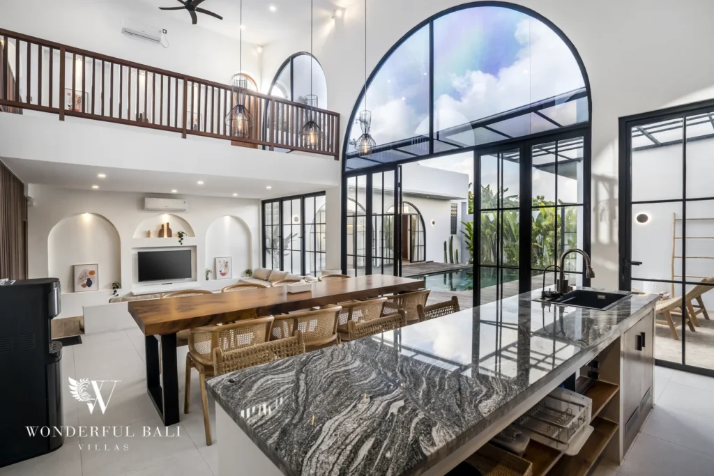 Kitchen with marble island and dining table under a double-height arched window in Pererenan, Bali