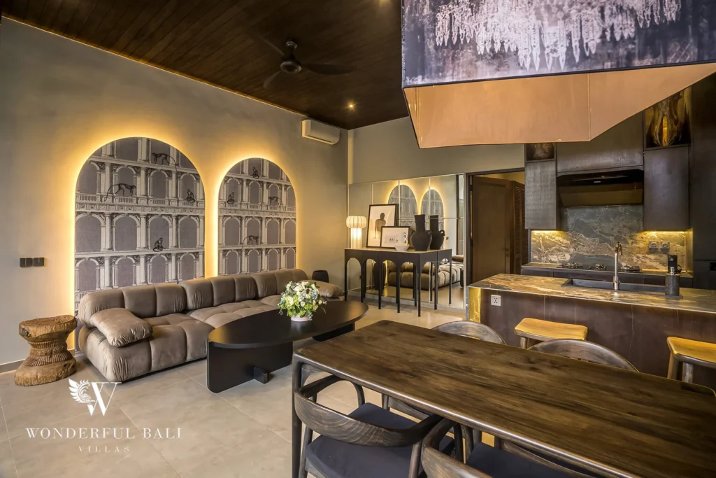 Living and dining space with sofa, arched murals and a wood table beneath a warmly lit kitchen at a 2-bedroom villa in Pererenan, Bali