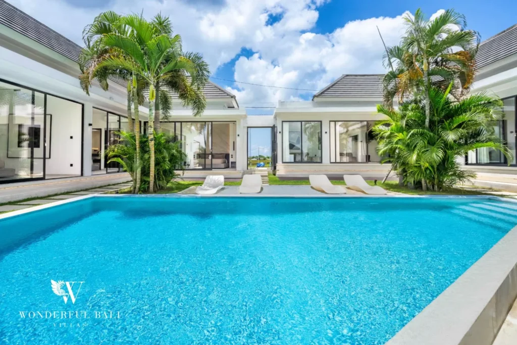 Bright pool courtyard with sun loungers and palms enclosed by the villa's glass-walled wings at a 5-bedroom villa in Pererenan, Bali